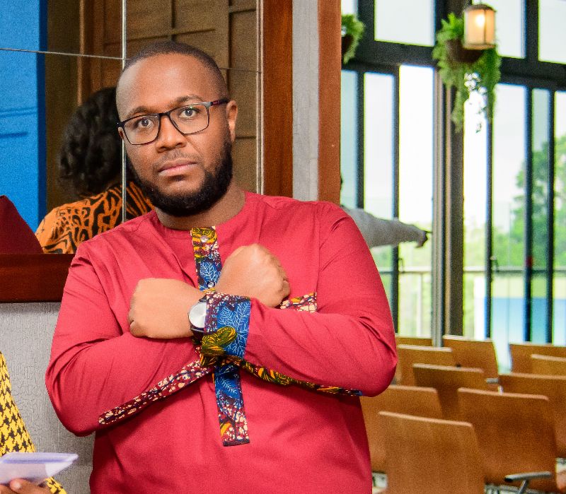 Philip Muigai standing with arms crossed in a red shirt with patterned trim at a This Is Digital community event