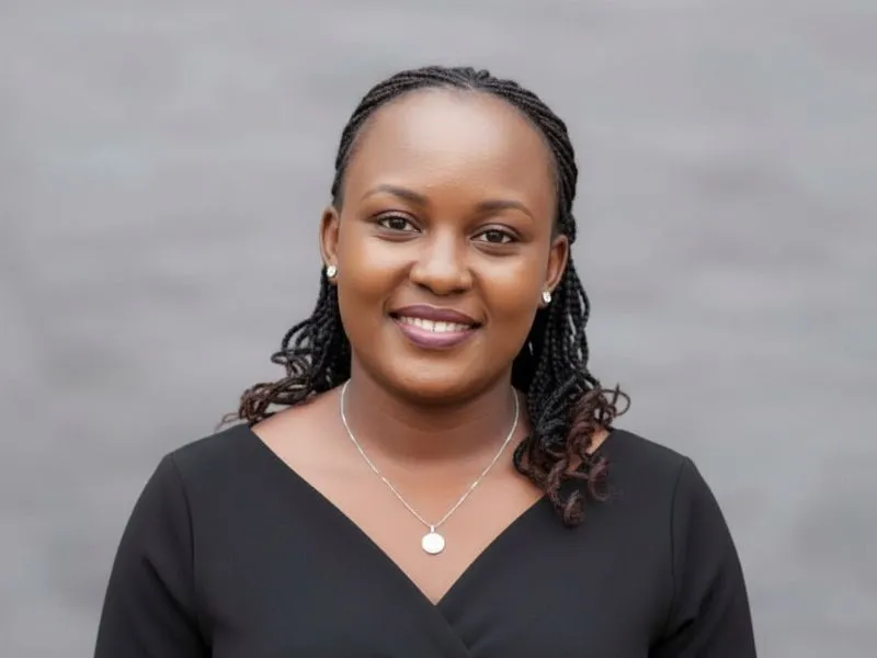 Carol Nyambura smiling in a black wrap dress and silver pendant necklace against a grey backdrop